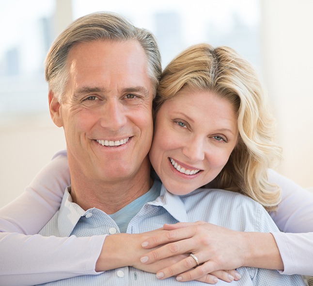 Older woman smiling, embracing man from behind at home